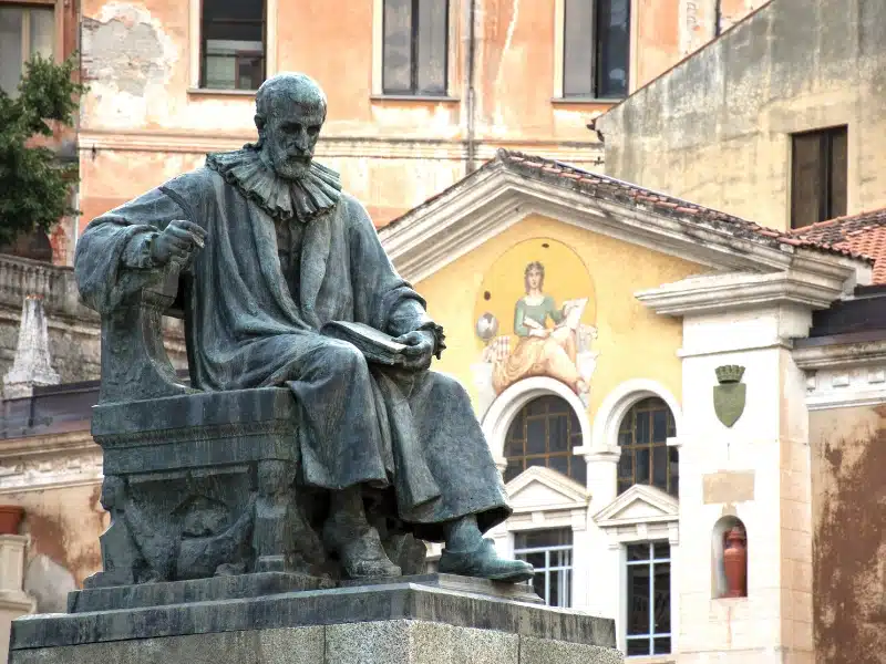 statue of a seated man in front of historic buildings