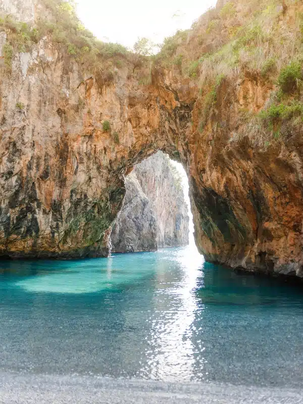 rock arch above turquoise water with a shingle beach in the foreground