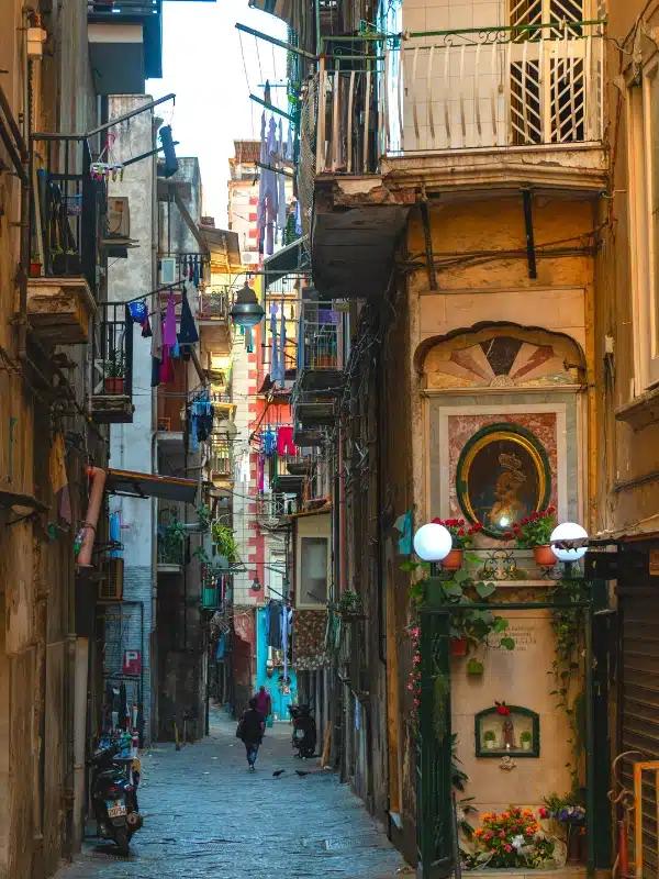 a narrow cobbled street in Naples with washong hanging from balconies