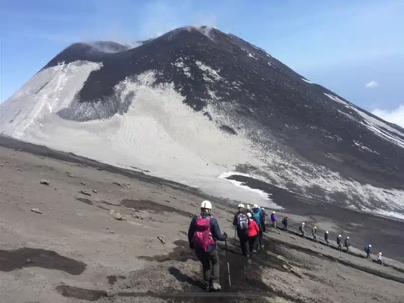 People wearing white helmets hiking down the slopes of Mount Etna