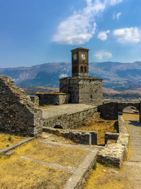 Stone castle with square clock tower with mountains in the far distance