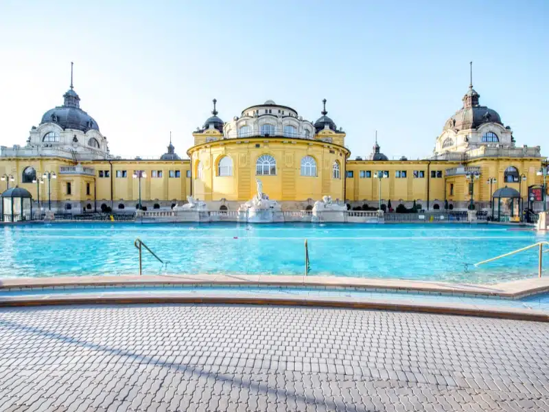 An image of the Szechenyi Thermal Baths in Budapest a grand yellow building with swimming baths in front