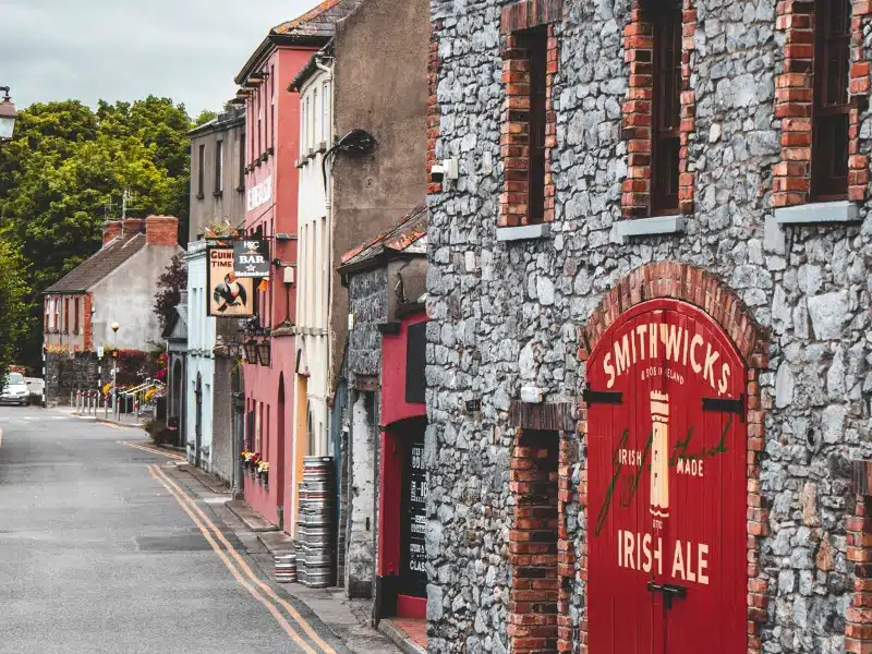 stone house with red arched door and metal beer barrels in the street