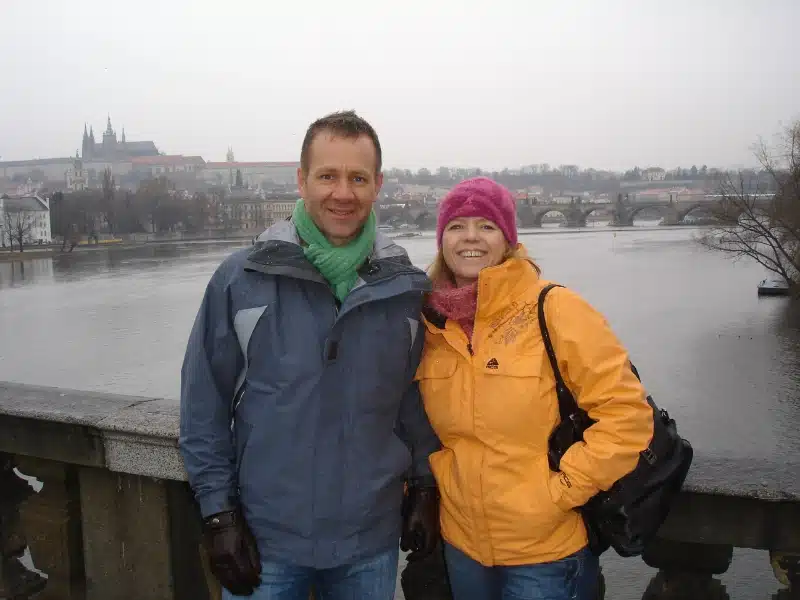 man and woman standing on a bridge over a river with a castle in the background