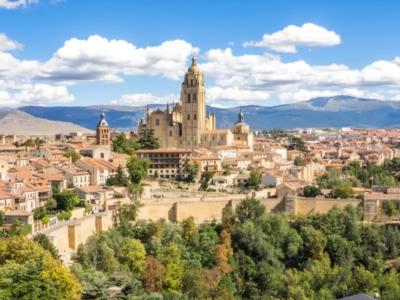 creamy colored buildlngs with terracotta roofs in a city with mountains in the background and trees in the foreground