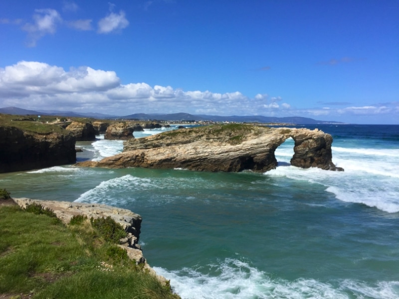 sea arch and other rocky features on a beach nacked by low grassy cliffs