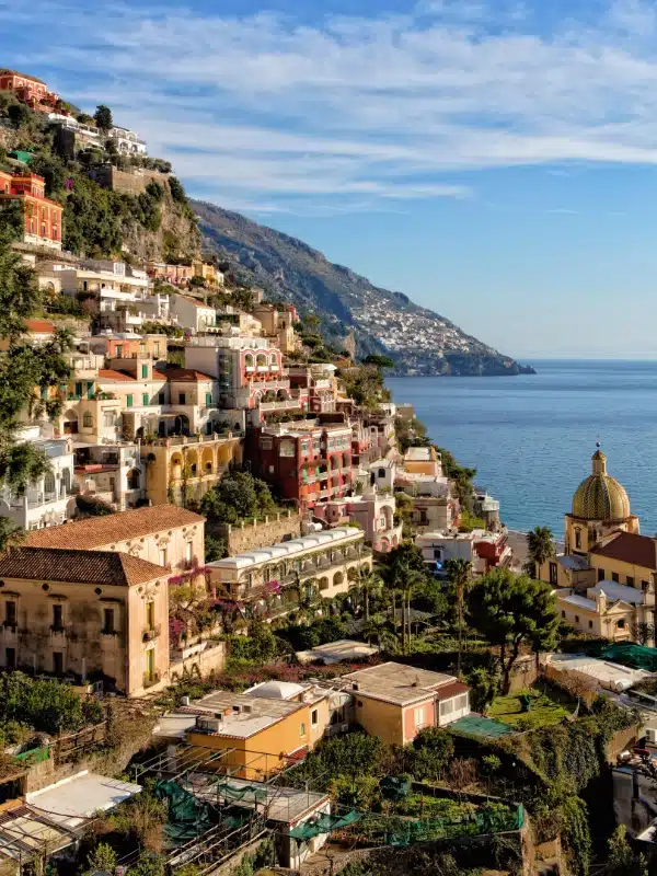 village of painted houses on a steep hillside with a domed church at the bottom facing the sea