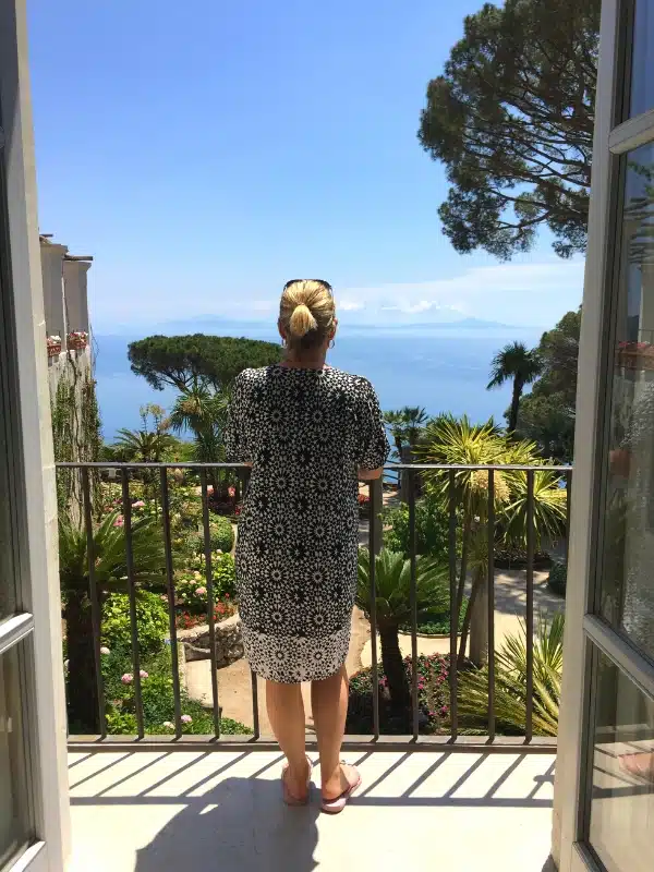 woman in black and white dress overlooking a lush garden of exotic plants and trees and a background of sea and blue sky