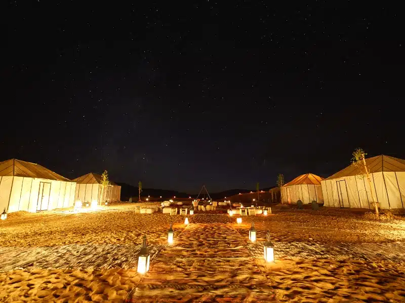 white tents in a desert with lanterns lighting a path to them