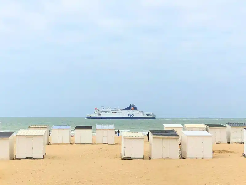 sand and beach huts with a large ferry in the distance