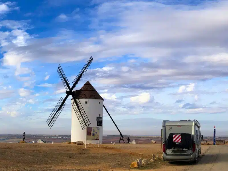 silver motorhome parked next to a traditional white Spanish windmill with a conical roof and slatted sails