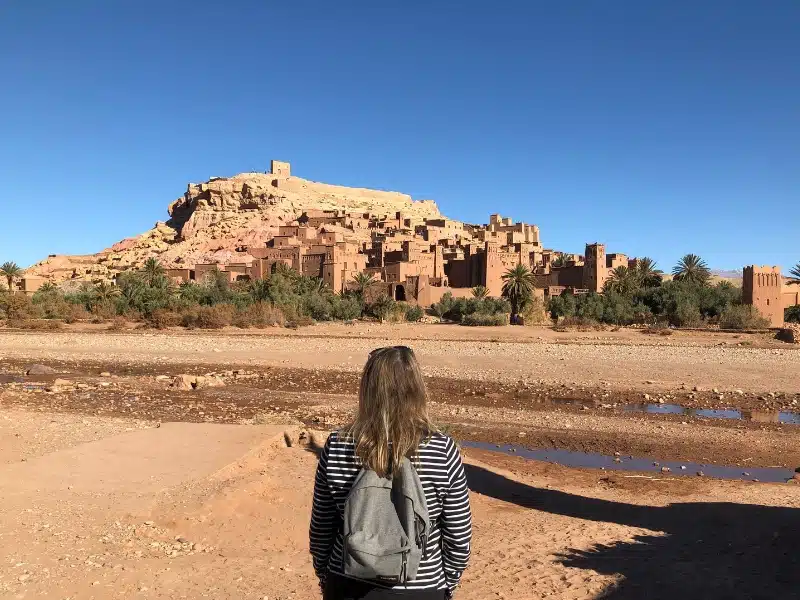 A woman looking at an ancient Berber village of mud huts over a dry river bed