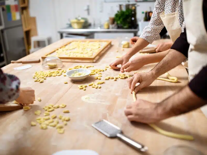 kitchen work surface with pasta and peoples hands rolling dough