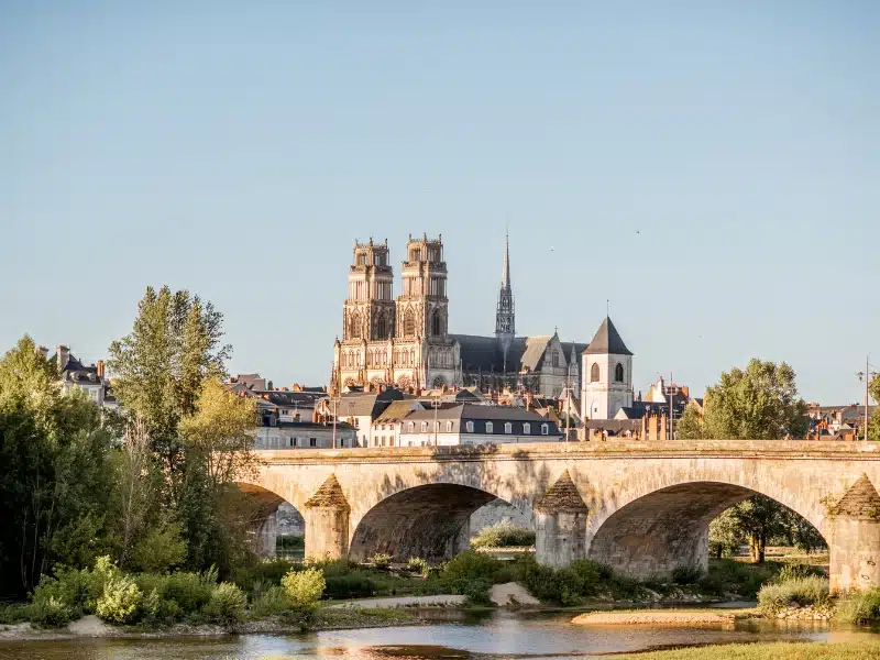 old stone arched bridge over a river with a twin towered cathedral in the background