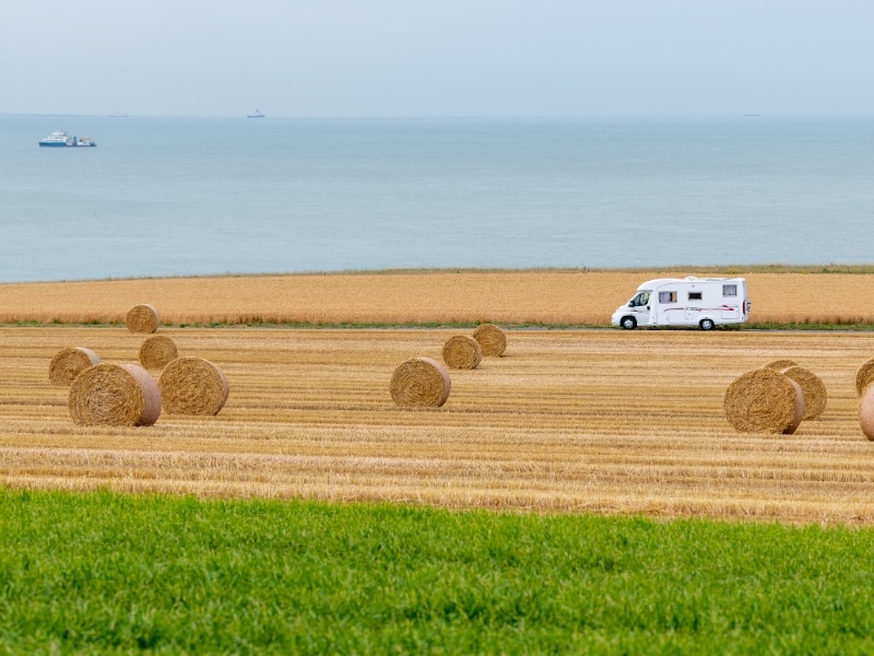 white motorhome driving between fields of wheat and grass with the English Channel in the distance
