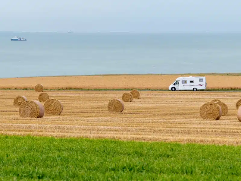 white motorhome driving between fields of wheat and grass with the English Channel in the distance