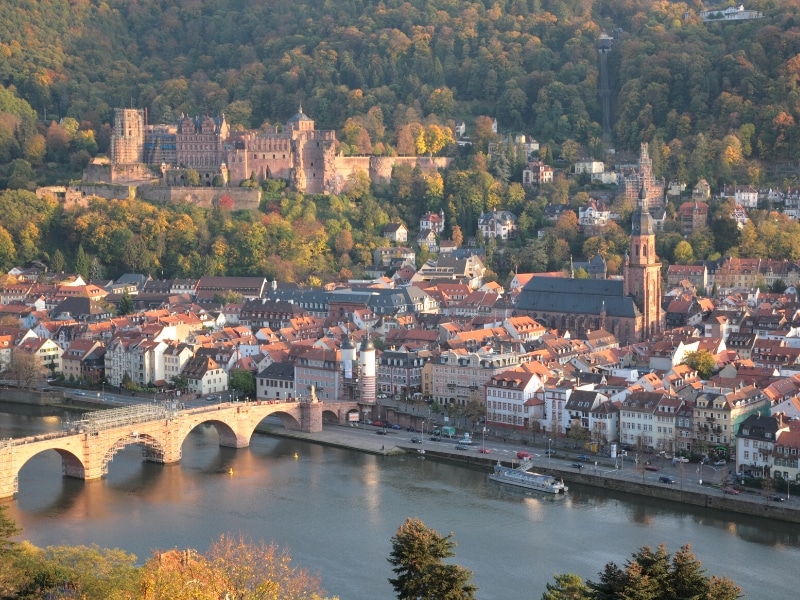 an arched bridge over a wide river leading to a town with a large church and castle on a hill