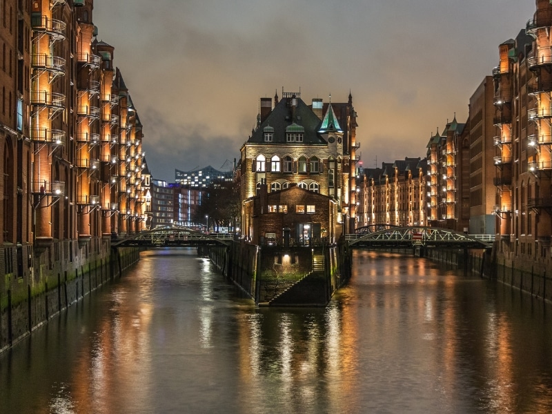 lit buildings rising from a river at night with a junction splitting the river in two