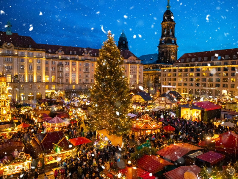 German christmas market in a square with fairy lights, red roofed stalls and a christmas tree