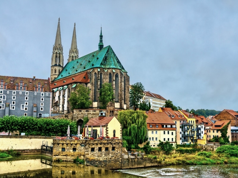 Ornate church with a gree copper roof with a river in the foreground