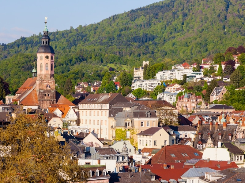 Historic buildings and a church with a wooded hilly backdrop