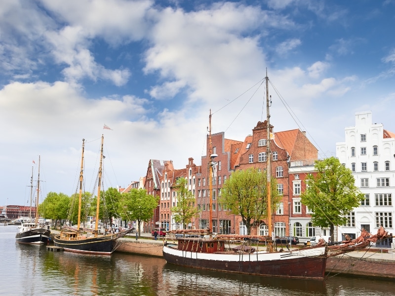 traditional sailing boats moored on a  river in front of historic red brick  houses