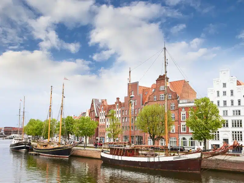 traditional sailing boats moored on a  river in front of historic red brick  houses