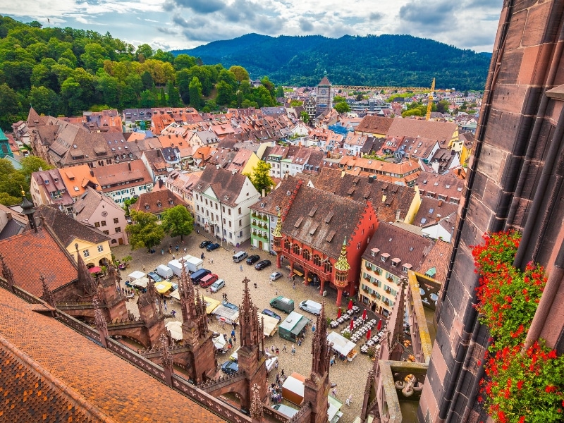 Square surrounded by medieval  buildings surrounded by an urban environment and further away trees