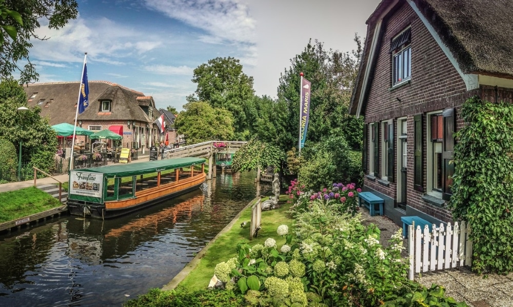 traditional thatched cottage on a canal with a tour boat