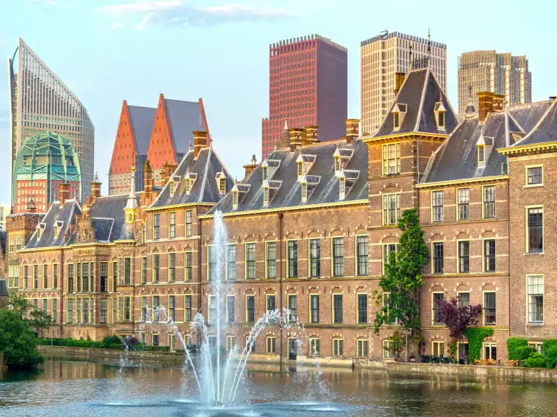 historic elegent tall buildings against a canal with a fountain with the tops of modern skyscrapers seen behind