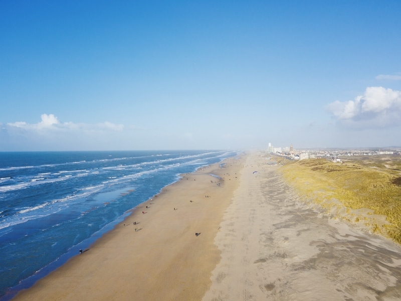 long sandy beach with the blue sea to one side and grassy dune to the other and a town of white buildings in the distance