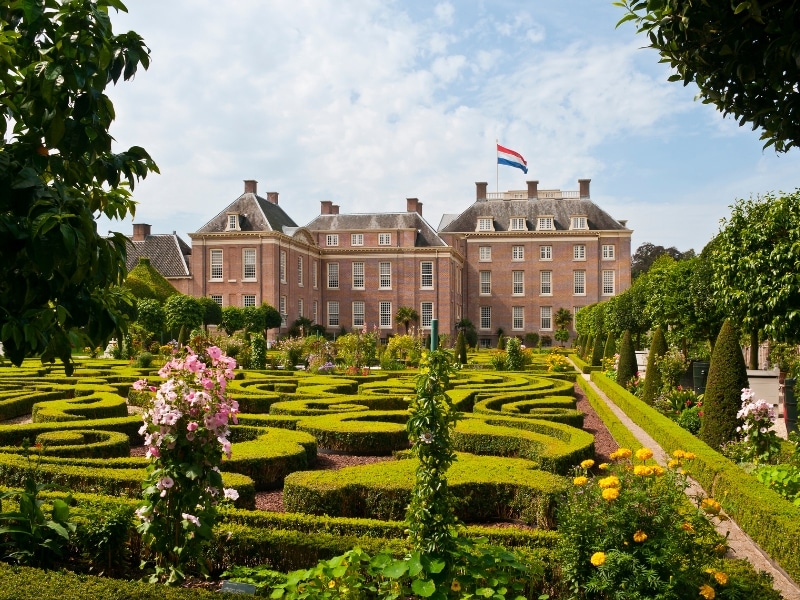 elegant palace with many windows behind a formal garden including manicured box hedging and trees