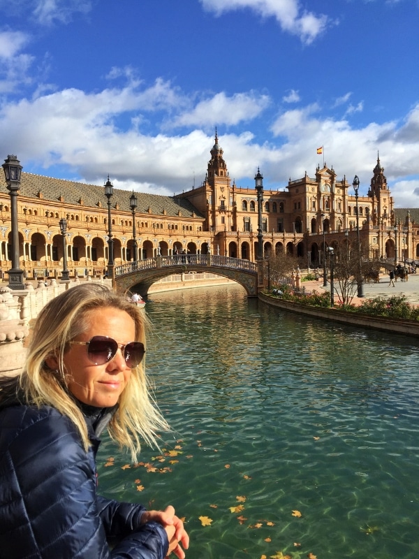 woman leaning on a bridge by water in front of an ornate building