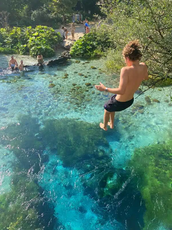 Person jumping into a deep pond of turquoise blue and green water