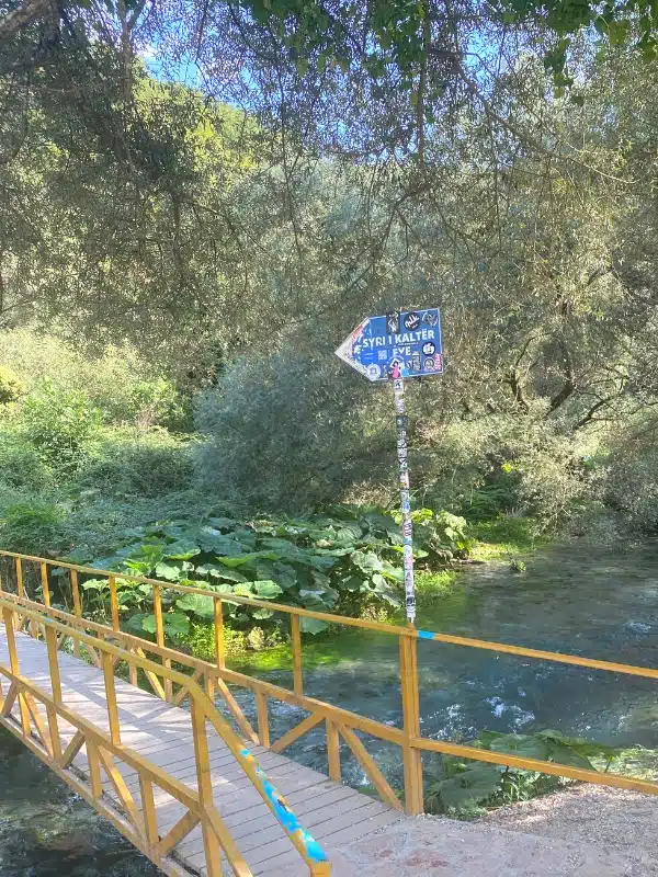 Blue sign on a yellow painted metal bridge across a river with lush vegetation