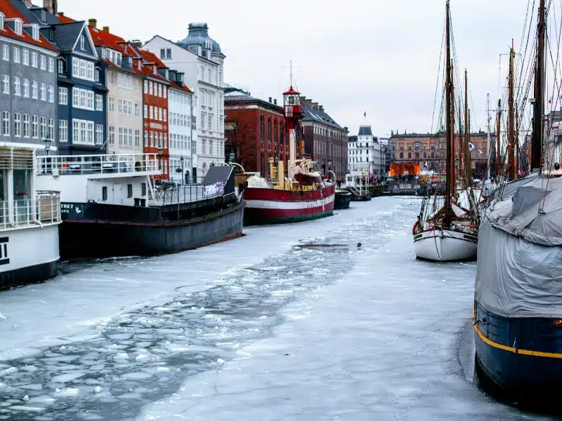 Ice covered canal lined with colorful boats and tall houses