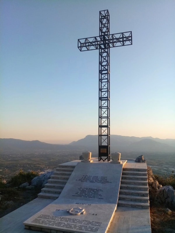 a large cross build of iron mounted on a stone platform with mountains in the background