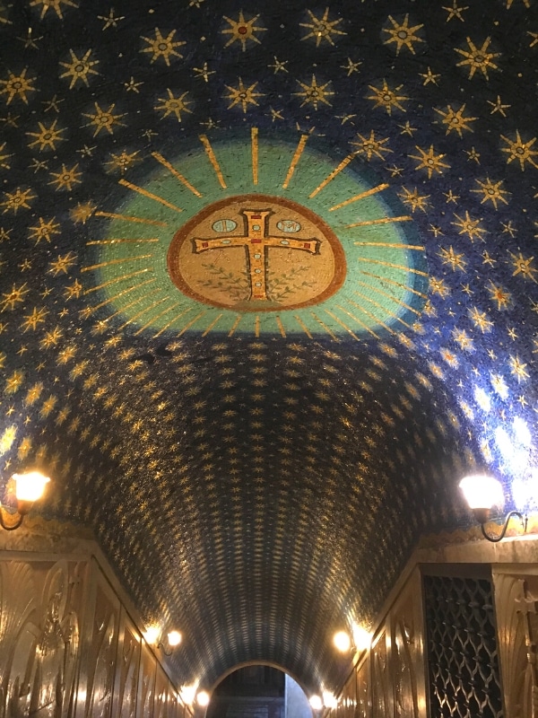 tunnel like ceiling painted in dark blue and lined with gold painted starts and a large gold cross in a green circle