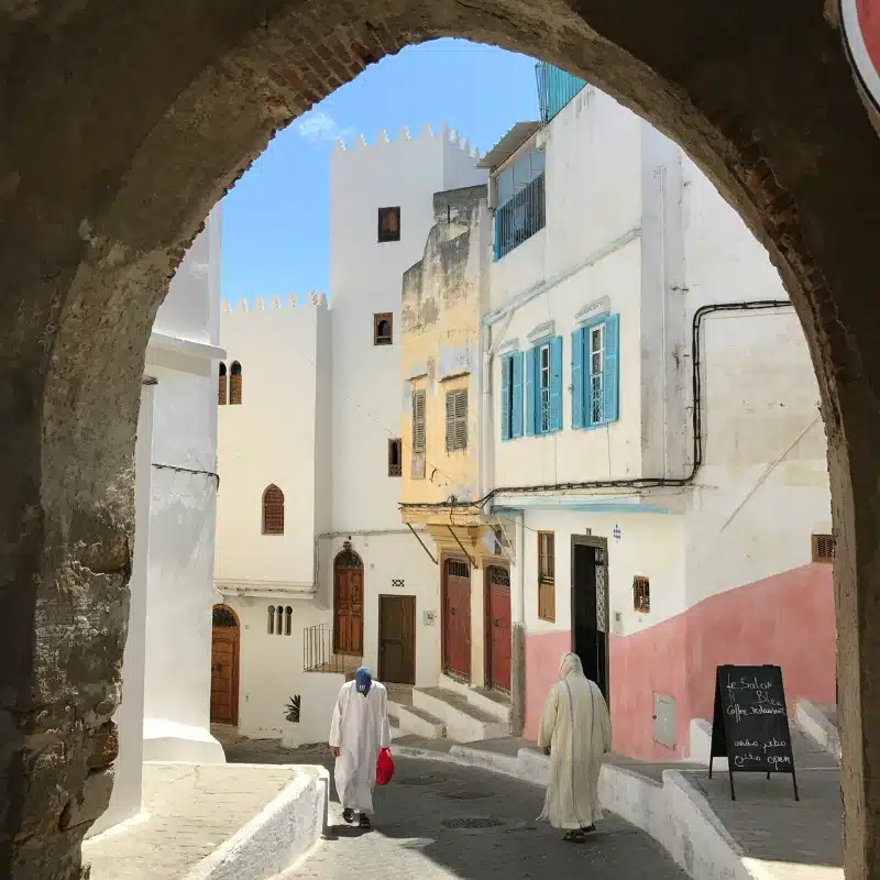 colorful buildings seen through a stone archyway, with men in traditional Moroccan dress walking past
