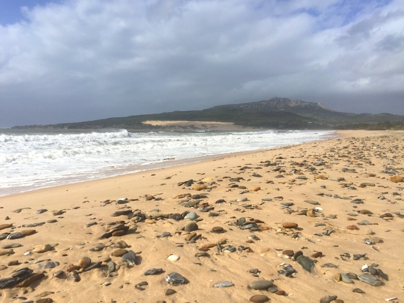 sandy beach with crashing waves and pebbles on a stormy day