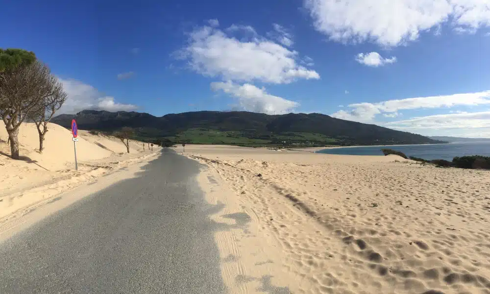 a road leading past a large sand dune and sea