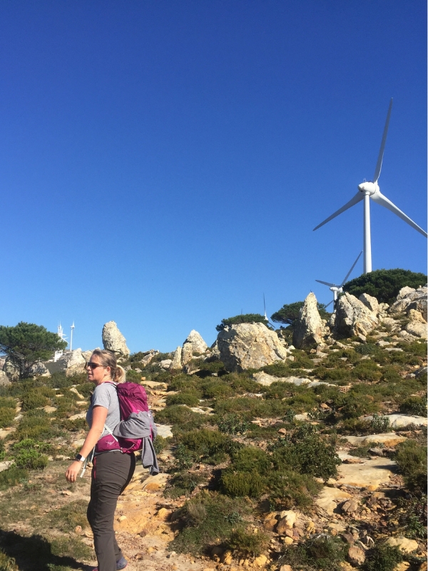 woman with pink rucksack hiking towards wind turbines on a rocky hill