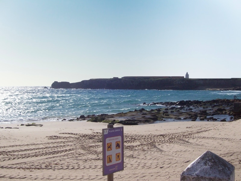 small beach area with sign and rock area looking towards a distant lighthouse