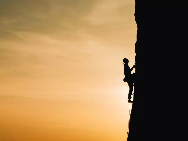 person climbing a rock face at sunset
