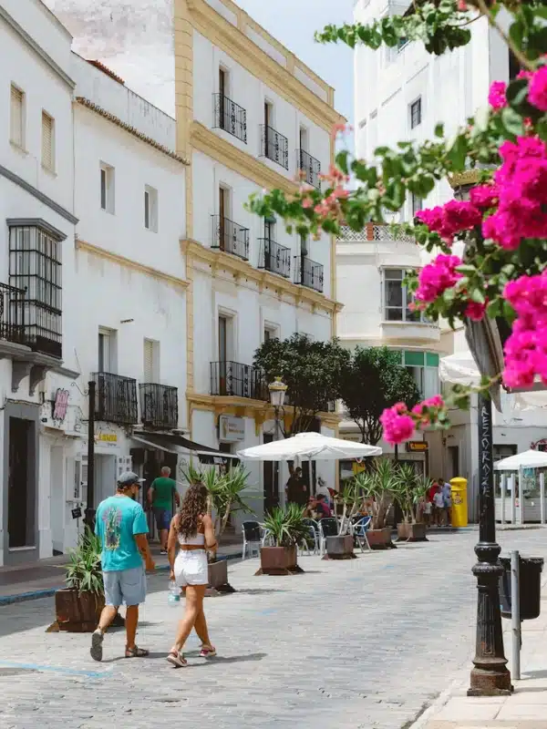 traditional white painted Spanish buildings with pots of flowers on the street and people walking along