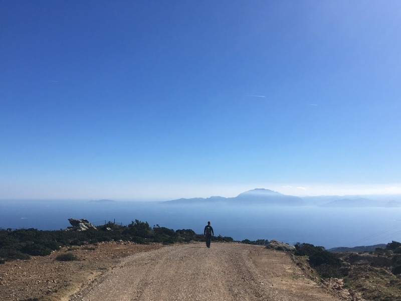 Man walking along a grave track with a view of the ocean and distant mountains