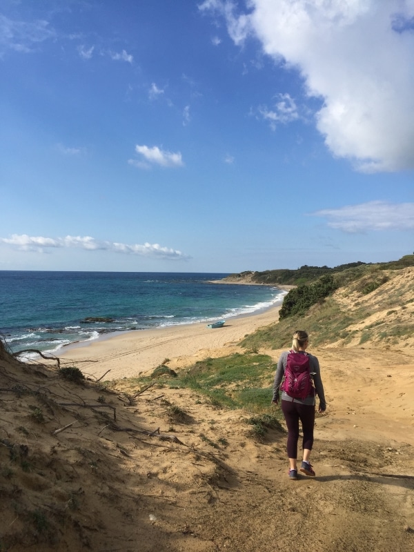 woman walking towards a sandy beach with a turquoise boat at the water's edge