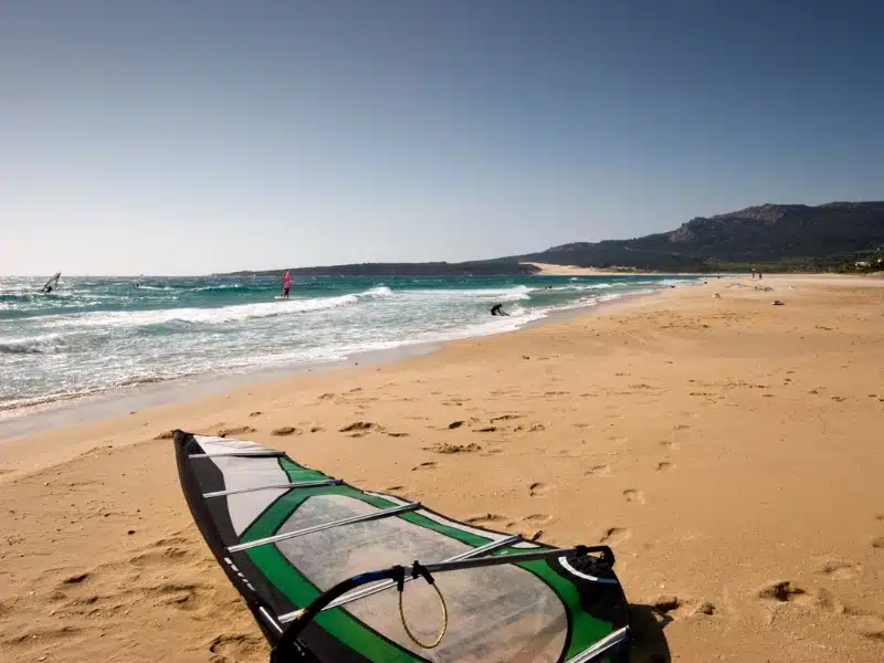 Green windsurf sail lying on a sandy beach 