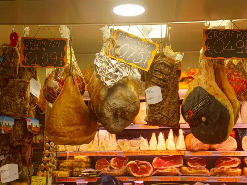 large whol hams haning above a counter with price labels attached