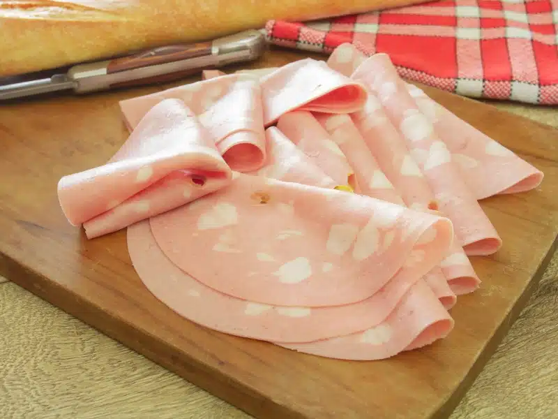 Mortadella arranged in a wooden chopping board with a red and white checked napkin